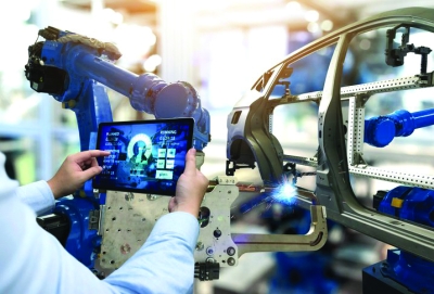 Engineer uses a digital tablet to control robotic arms assembling a car frame in a high-tech manufacturing environment.