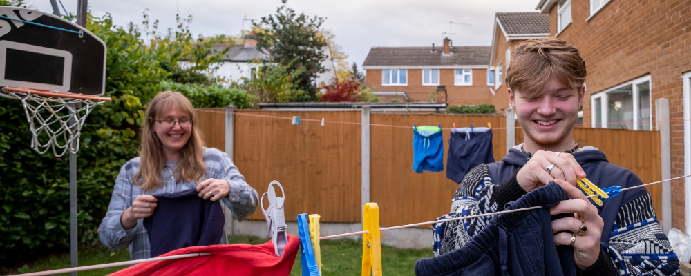 Image shows a women smiling, showing a teenager how to put their washing out