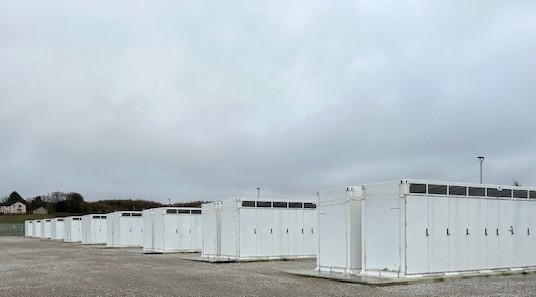 Image of a battery site. There are rows of white structures, with vents near the top.