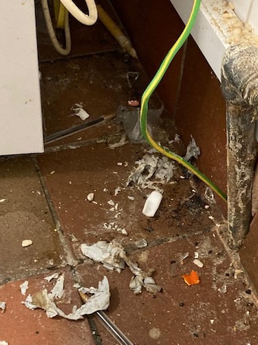 A photo of a section of floor, within Chiltern View Care Home. The floor is covered with dirt and a loose wire hangs down by the wall.