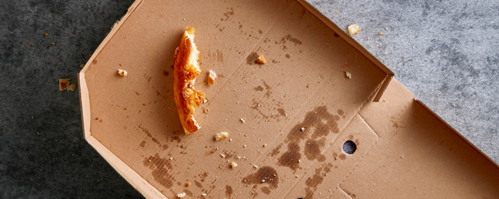 A pizza box with a single crust, some crumbs and grease marks in it.