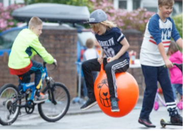 A child on a Space Hopper with other children on bicycles.