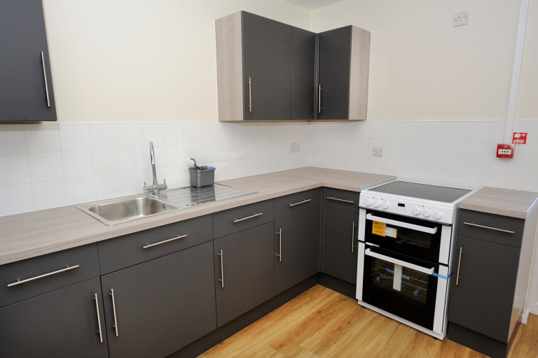 Modern fitted kitchen in Croft Green with grey cabinets, integrated oven, sink and wood-effect flooring.