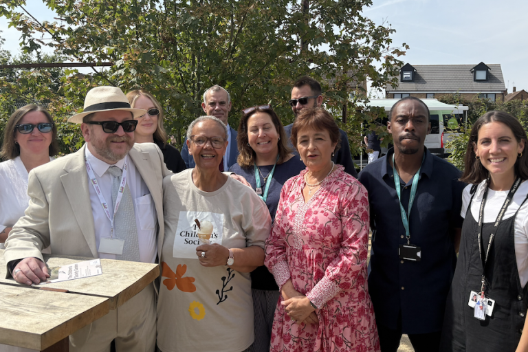 Group of ten people posing outdoors in a garden on a sunny day, gathered around a high table at Leighton Buzzard Youth Centre.