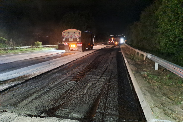 Road resurfacing at night, with construction vehicles working on a stripped section of carriageway.
