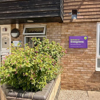 Entrance to Evergreen Step-up Step-down Unit, with a purple welcome sign, brick façade and raised flower bed.