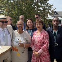Group of ten people posing outdoors in a garden on a sunny day, gathered around a high table at Leighton Buzzard Youth Centre.