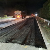 Road resurfacing at night, with construction vehicles working on a stripped section of carriageway.