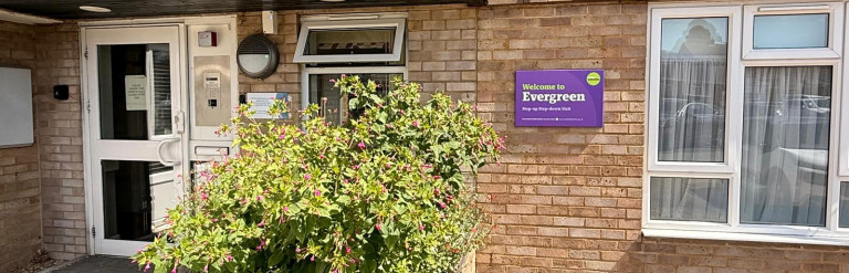 Entrance to Evergreen Step-up Step-down Unit, with a purple welcome sign, brick façade and raised flower bed.